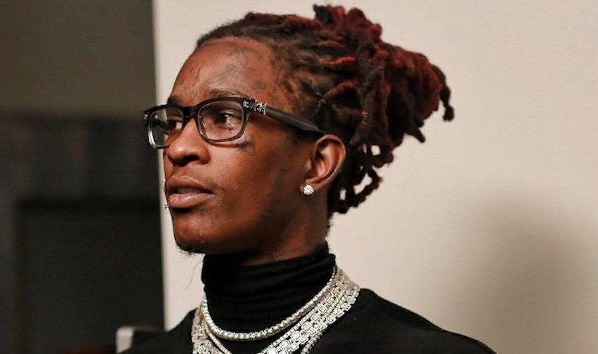 Young Thug mengenakan kaus hitam, dengan kalung berwarna putih, kacamata hitam, dan rambut yang diikat.